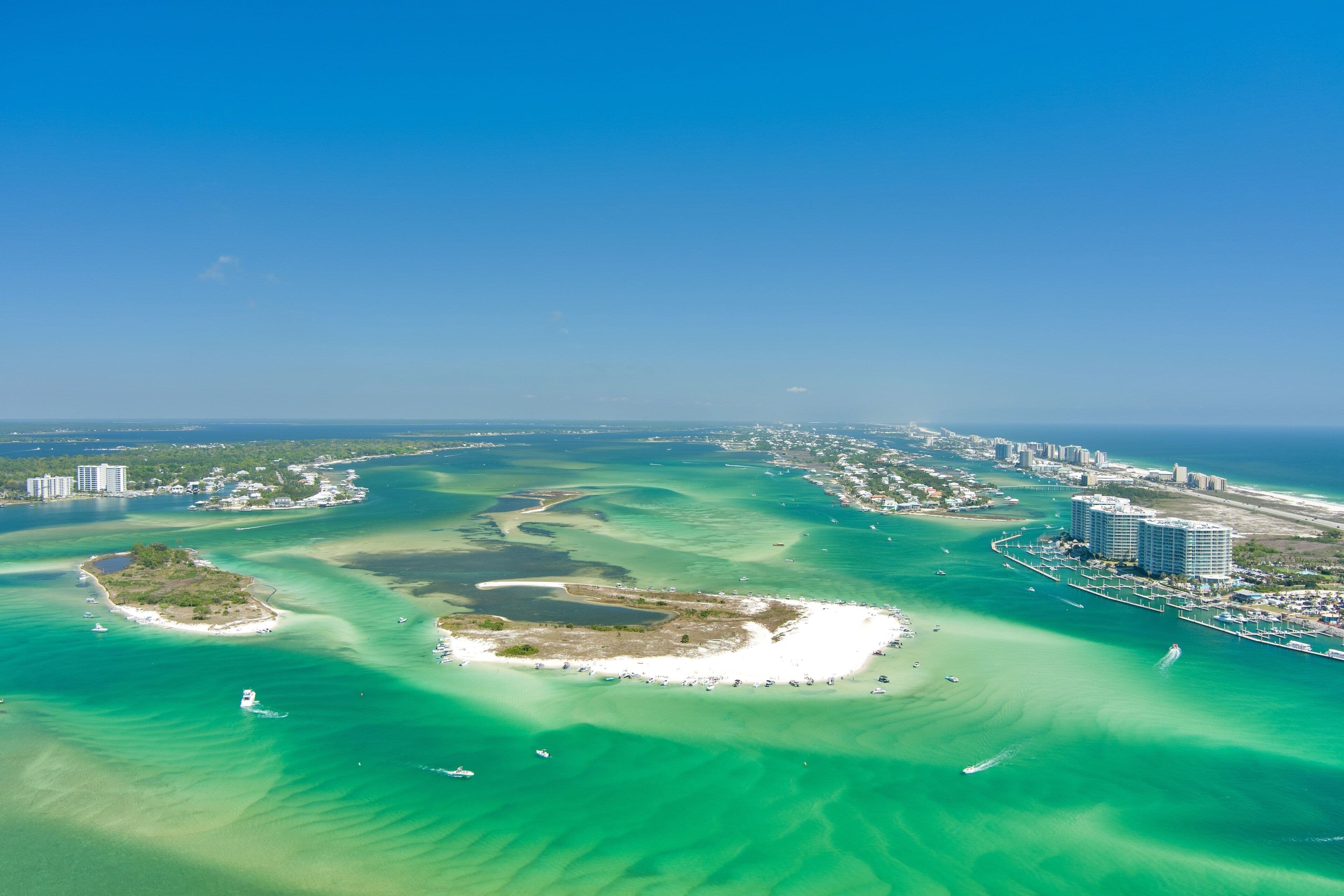 Aerial view of the Alabama Gulf Coast: turquoise water and shifting sandbars around a white sand island, with condominiums lining the shore beyond