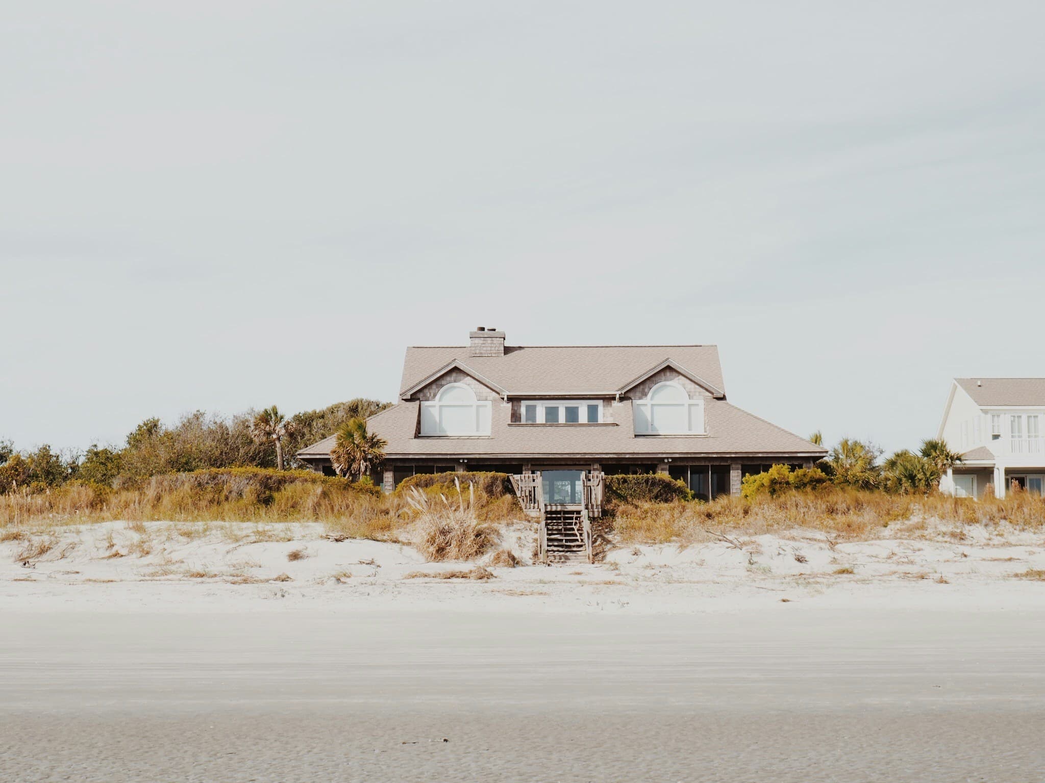 A shingled beach house behind dune grass, with steps leading down to the sand